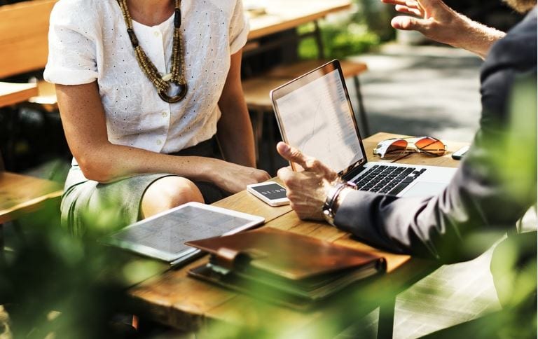 B2B Marketing: imagem de duas pessoas pessoas vestidas com roupa de trabalho conversando com um notebook na mesa.