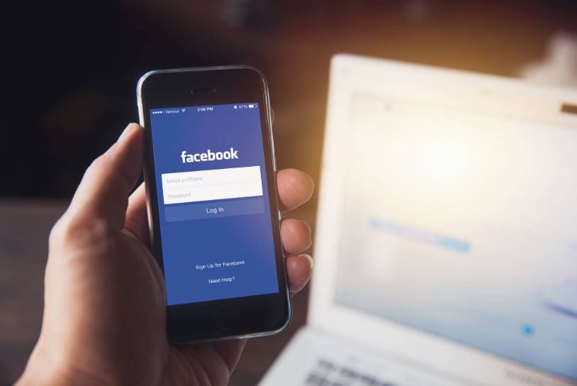 Facebook para negócios: imagem de uma mão segurando o celular com a tela de login do Facebook aparecendo.