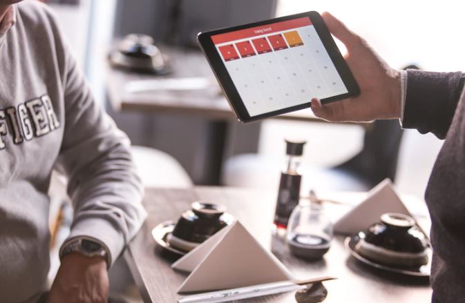 Calendário de Marketing: imagem de duas pessoas em reunião, uma delas está segurando um tablet com a tela aberta em um calendário online