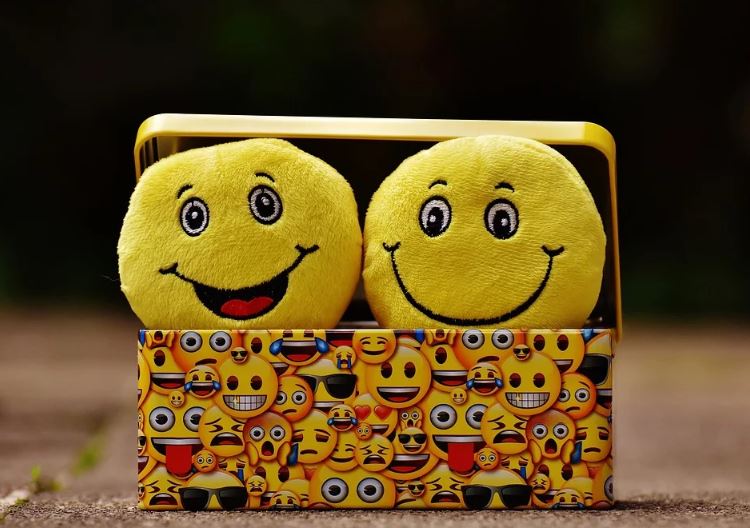 Emojis no marketing: imagem de dois emojis com sorriso apoiados em uma caixa estampada de emojis pequenos.
