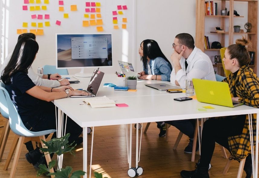 Plano de marketing digital: imagem de uma sala de reunião com várias pessoas sentadas conversando sobre negócios olhando para uma parede de post it coloridos