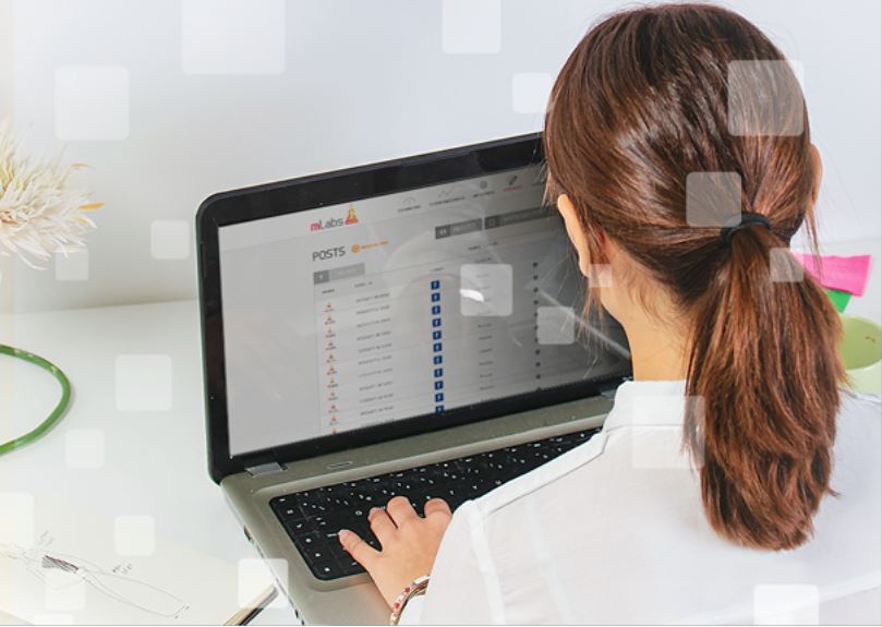 postagem automatica instagram: imagem de uma mulher sentada digitando em um notebook com a página de posts da mLabs aparecendo na tela