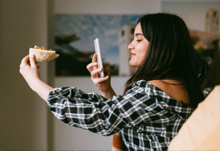 O que e UGC: na foto, uma moça branca está segurando o celular e apontando para uma pão segurada por sua outra mão. Ela está fotografando a comida.