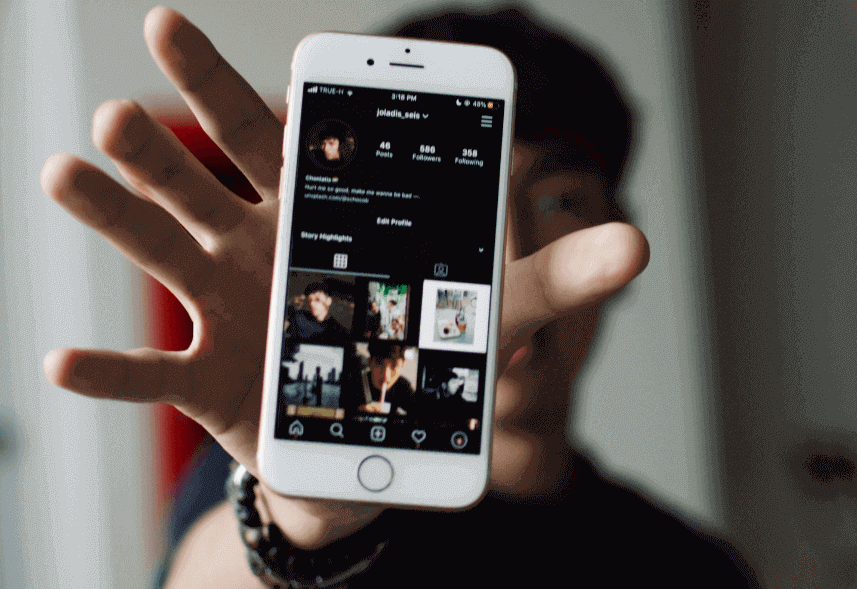 beneficios das redes sociais: imagem de um homem jovem com a mão aberta soltando um celular, na tela do aparelho aparece o Instagram