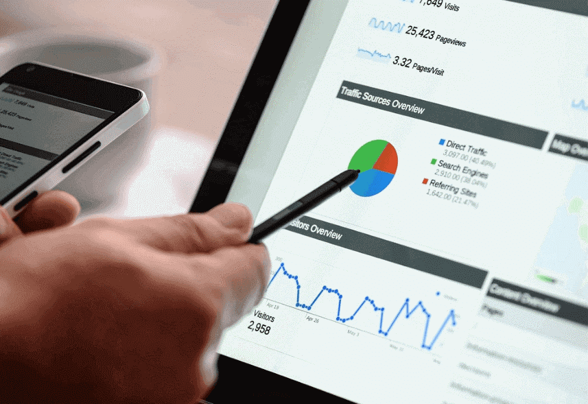 o que e google analytics: imagem de uma mão segurando uma caneta apontando para a tela de um notebook com imagens de gráficos aparecendo no monitor