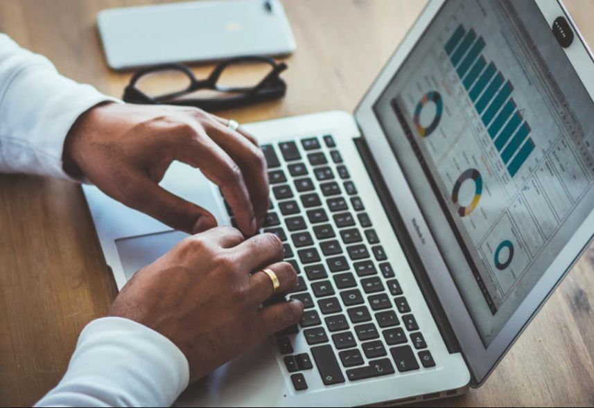 Relatório Google Ads: imagem das mãos de um homem usando o notebook. Na tela, aparecem alguns gráficos em formato de barra e de pizza.